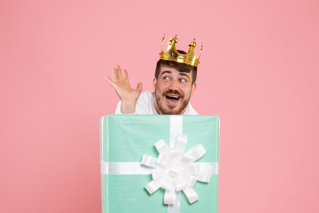 Front view of young man inside present box with crown on a pink wall
