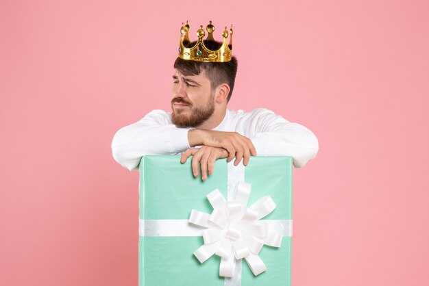 Вид спереди молодого человека внутри настоящей коробки с короной на розовой стене