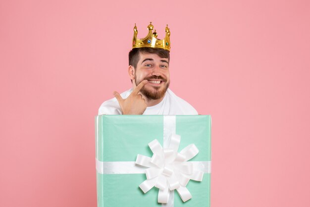Front view of young man inside present box with crown on pink wall