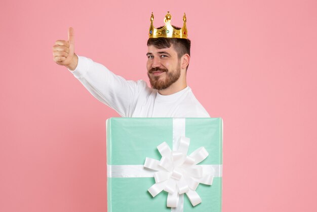 ピンクの壁に王冠とプレゼントボックス内の若い男の正面図