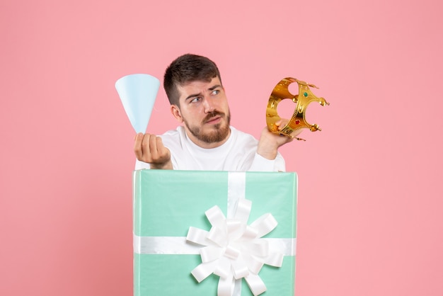 Front view of young man inside present box with crown on pink wall