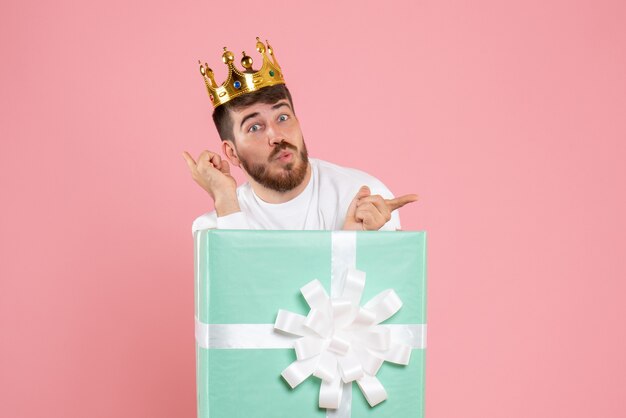 Front view of young man inside present box with crown on pink wall