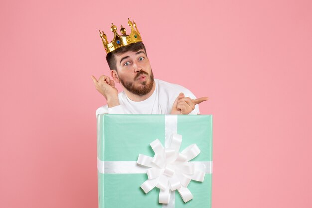 ピンクの壁に王冠とプレゼントボックス内の若い男の正面図