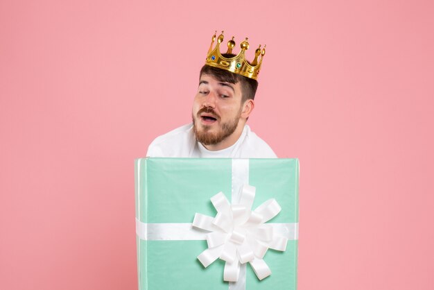 Front view of young man inside present box with crown on the pink wall