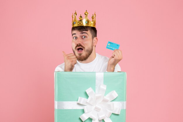 Front view of young man inside present box with crown on the pink wall