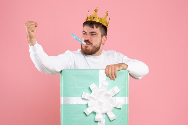 Front view of young man inside present box with crown threatening someone on pink wall