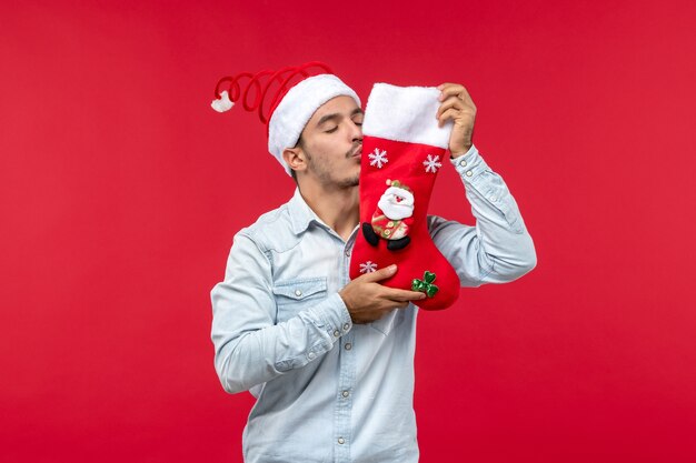 赤い壁にクリスマスの靴下にキスする若い男の正面図