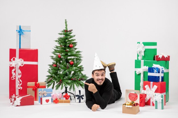 Front view of young man laying around holiday presents on the white wall