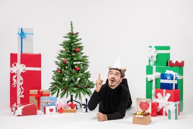 Front view of young man laying around holiday presents on white wall