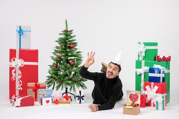 Front view of young man laying around holiday presents on white wall