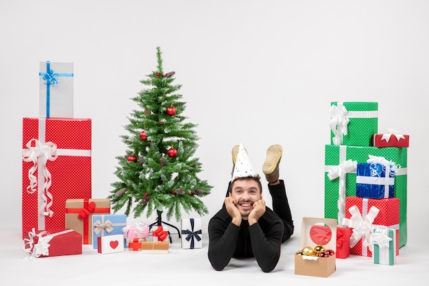 白い壁に笑顔で休日のプレゼントの周りに横たわっている若い男の正面図