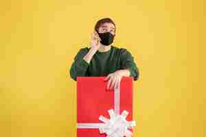 Free photo front view young man looking up standing behind big giftbox on yellow