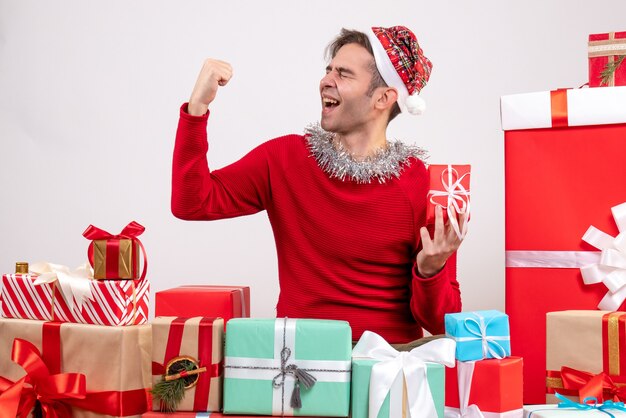Front view young man making winning gesture sitting around xmas gifts