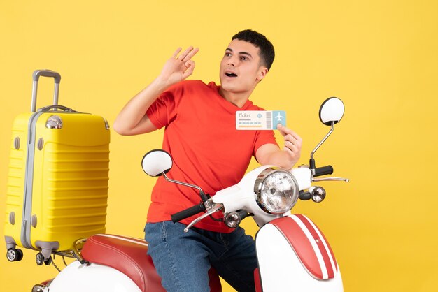 Front view young man on moped holding ticket looking at something on yellow background