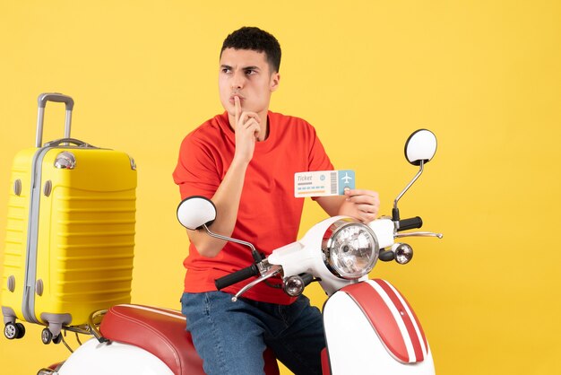 Front view young man on moped holding ticket making hush sign