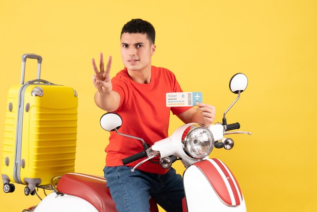 Front view young man on moped holding ticket showing three fingers