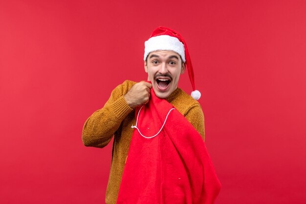 Front view of young man opening present bag on a red wall