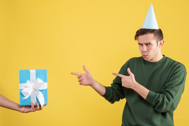 Front view young man pointing at gift in human hand on yellow 