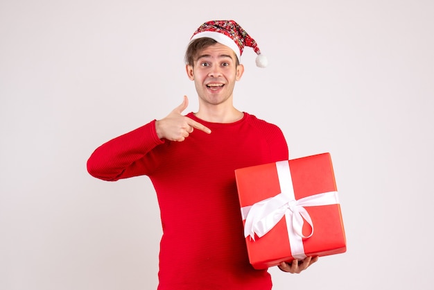 Front view young man pointing at gift standing on white 