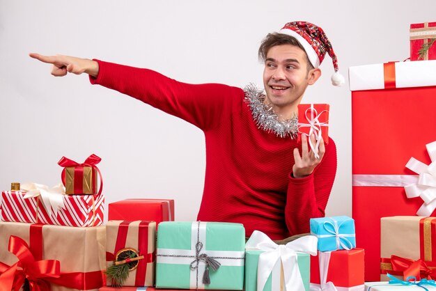 Вид спереди молодой человек, указывая на что-то сидя вокруг рождественских подарков