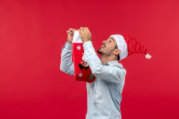 Front view of young man posing with big sock on red wall