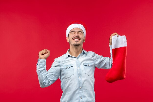Front view of young man posing with christmas sock on a red wall
