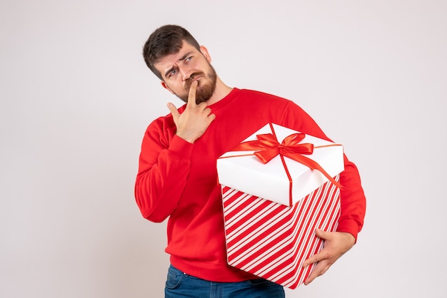 흰 벽에 상자 생각에 크리스마스 선물을 들고 빨간 셔츠에 젊은 남자의 전면보기