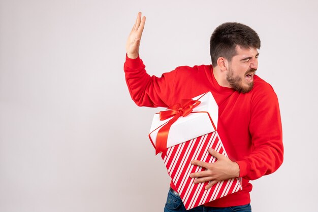 Front view of young man in red shirt holding christmas present in box on white wall