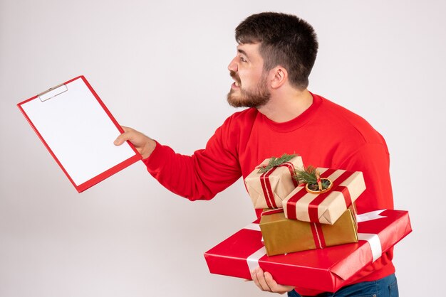 Front view of young man in red shirt holding christmas presents arguing on a white wall