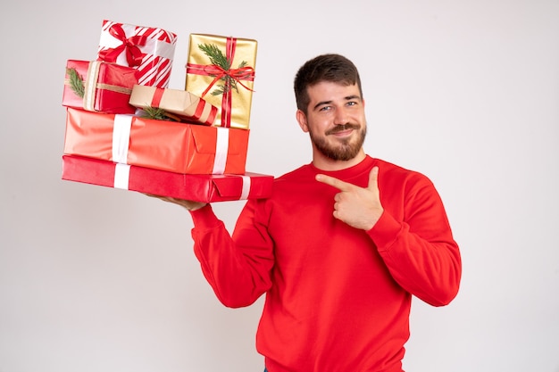 Front view of young man in red shirt holding christmas presents on white wall