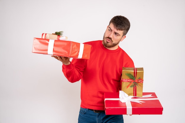 Front view of young man in red shirt holding christmas presents on white wall