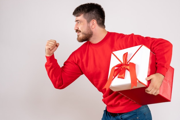 흰 벽에 상자에 크리스마스 선물을 들고 빨간 셔츠에 젊은 남자의 전면보기