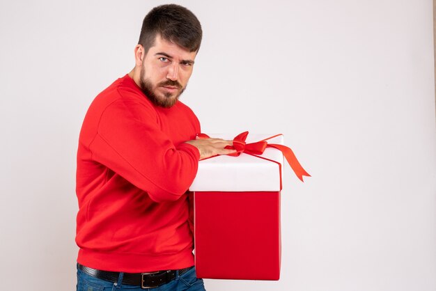 Вид спереди молодого человека в красной рубашке, держащего рождество в коробке на белой стене