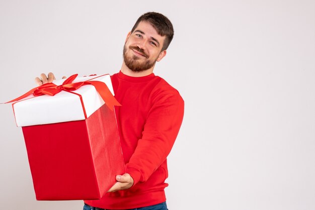 Front view of young man in red shirt holding xmas present in box on white wall