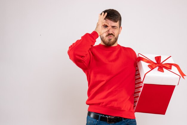 흰 벽에 상자에 크리스마스 선물을 들고 빨간 셔츠에 젊은 남자의 전면보기