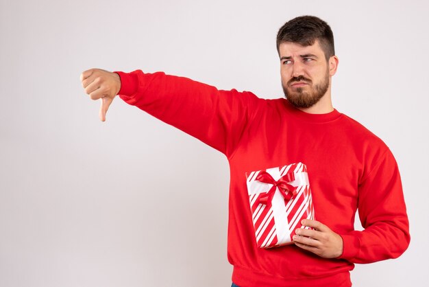 Front view of young man in red shirt holding xmas present on white wall