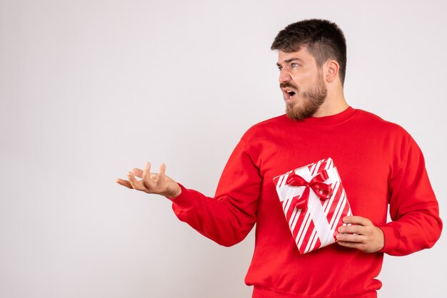 Front view of young man in red shirt holding xmas present on white wall