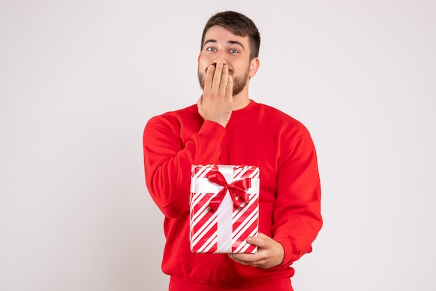 Front view of young man in red shirt holding xmas present on white wall