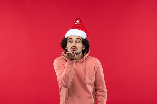 Front view of young man sending air kisses on red wall