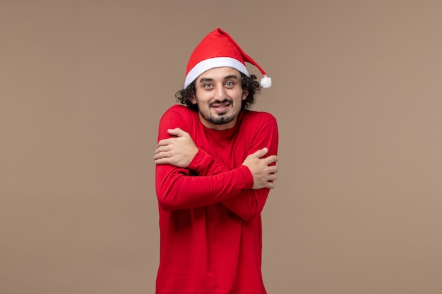 Вид спереди молодого человека, дрожащего от холода на коричневом фоне, рождественские эмоции, праздник