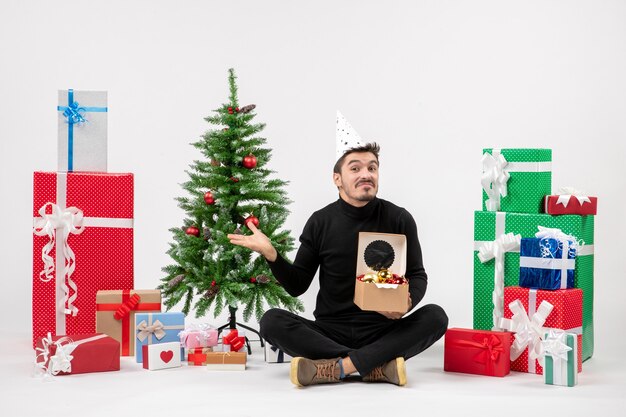 휴일 주위에 앉아 젊은 남자의 전면보기 흰 벽에 나무 장난감을 들고 선물
