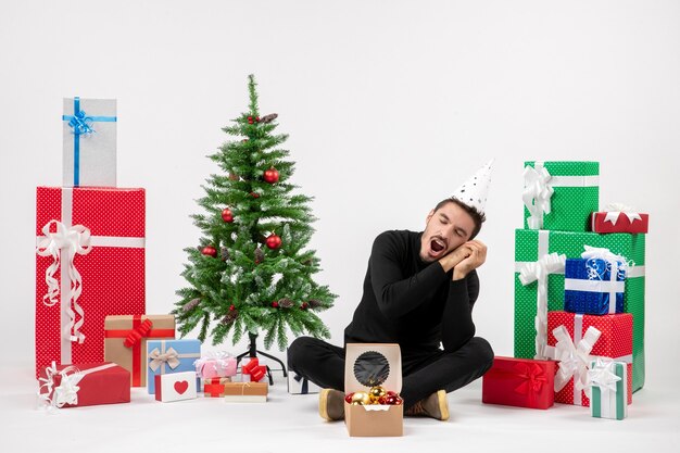 휴일 선물 주위에 앉아 흰 벽에 하품 젊은 남자의 전면보기
