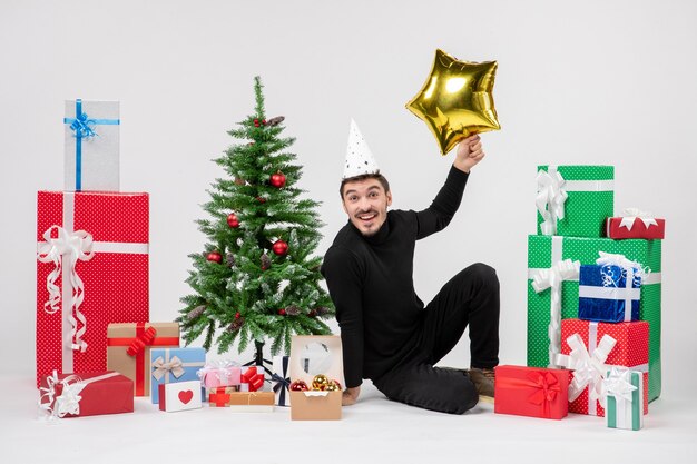 Front view of young man sitting around presents and holding gold star figure on a white wall