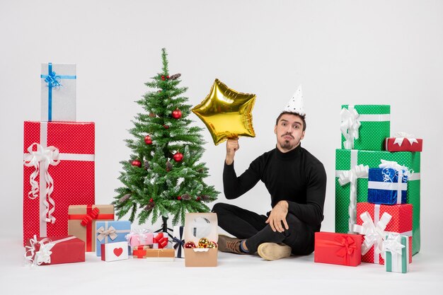 Front view of young man sitting around presents and holding gold star figure on a white wall