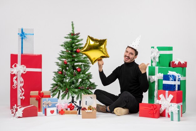 Front view of young man sitting around presents and holding gold star figure on a white wall