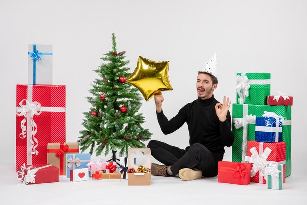 Front view of young man sitting around presents and holding gold star figure on the white wall