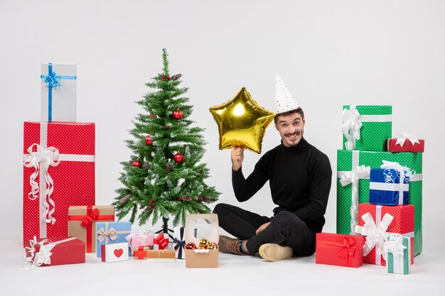 Front view of young man sitting around presents and holding gold star figure on the white wall