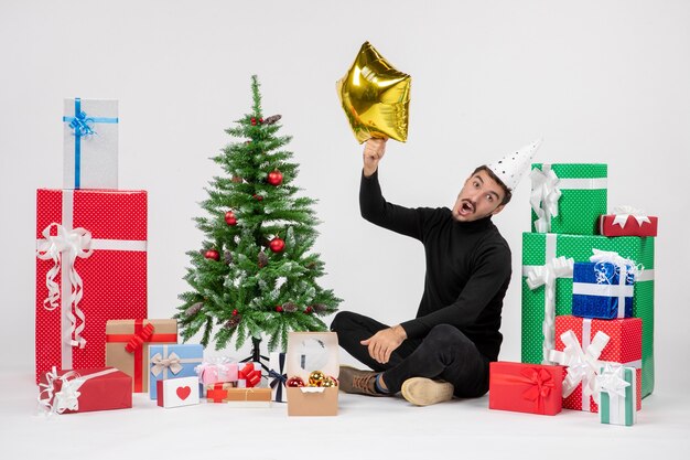 Front view of young man sitting around presents and holding gold star figure on the white wall