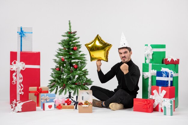 Front view of young man sitting around presents and holding gold star figure on white wall