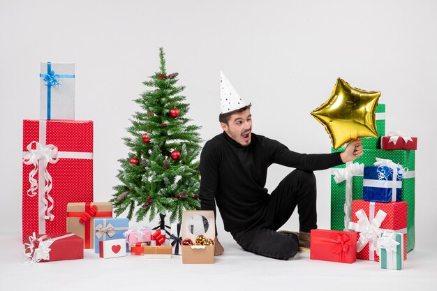 Front view of young man sitting around presents and holding gold star figure on white wall